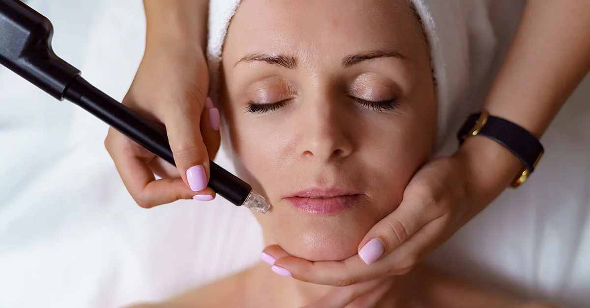 Vue du docteur cosmétologue effectuant une procédure anti-âge dans le bureau de cosmétologie. Femme satisfaite au chapeau jetable allongée sur le canapé et se relaxant