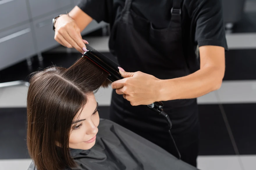 Coiffeur professionnel utilisant un lisseur sur les cheveux d'une cliente dans un salon de beauté