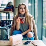 Femme assise confortablement avec une tasse de thé, des livres et des suppléments de vitamines, illustrant le bien-être mental