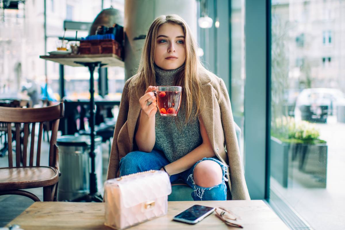 Femme assise confortablement avec une tasse de thé, des livres et des suppléments de vitamines, illustrant le bien-être mental