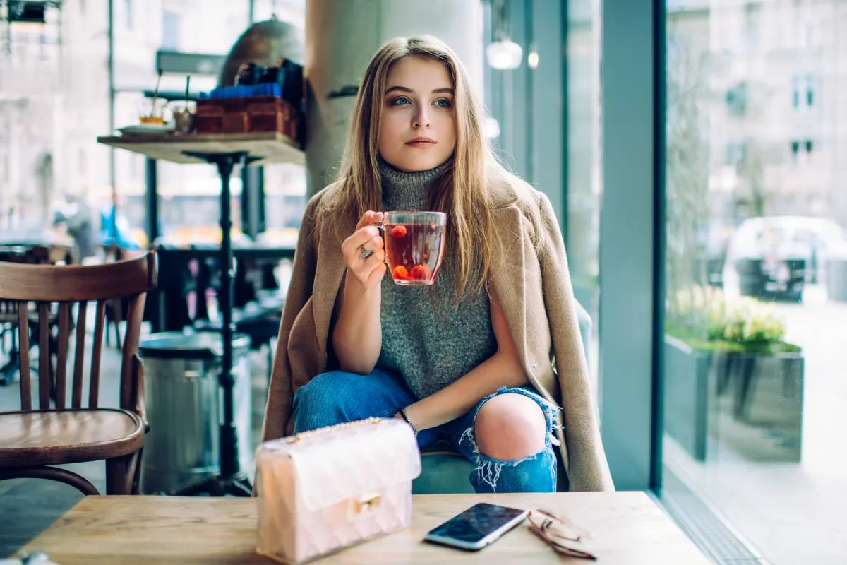 Femme assise confortablement avec une tasse de thé, des livres et des suppléments de vitamines, illustrant le bien-être mental
