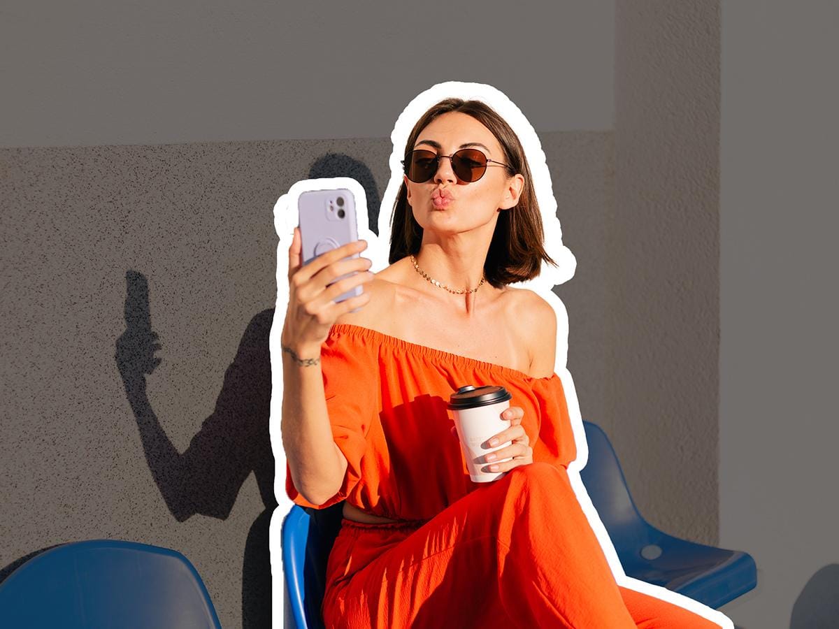 Femme confiante à la coupe courte prenant un selfie, portant une robe orange vif et des lunettes de soleil, tenant un café - parfaite illustration d'une transition capillaire réussie pour la rentrée
