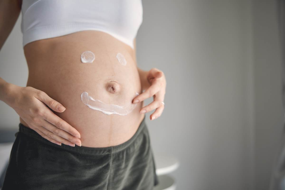 Femme enceinte appliquant une crème avec un sourire dessiné sur son ventre