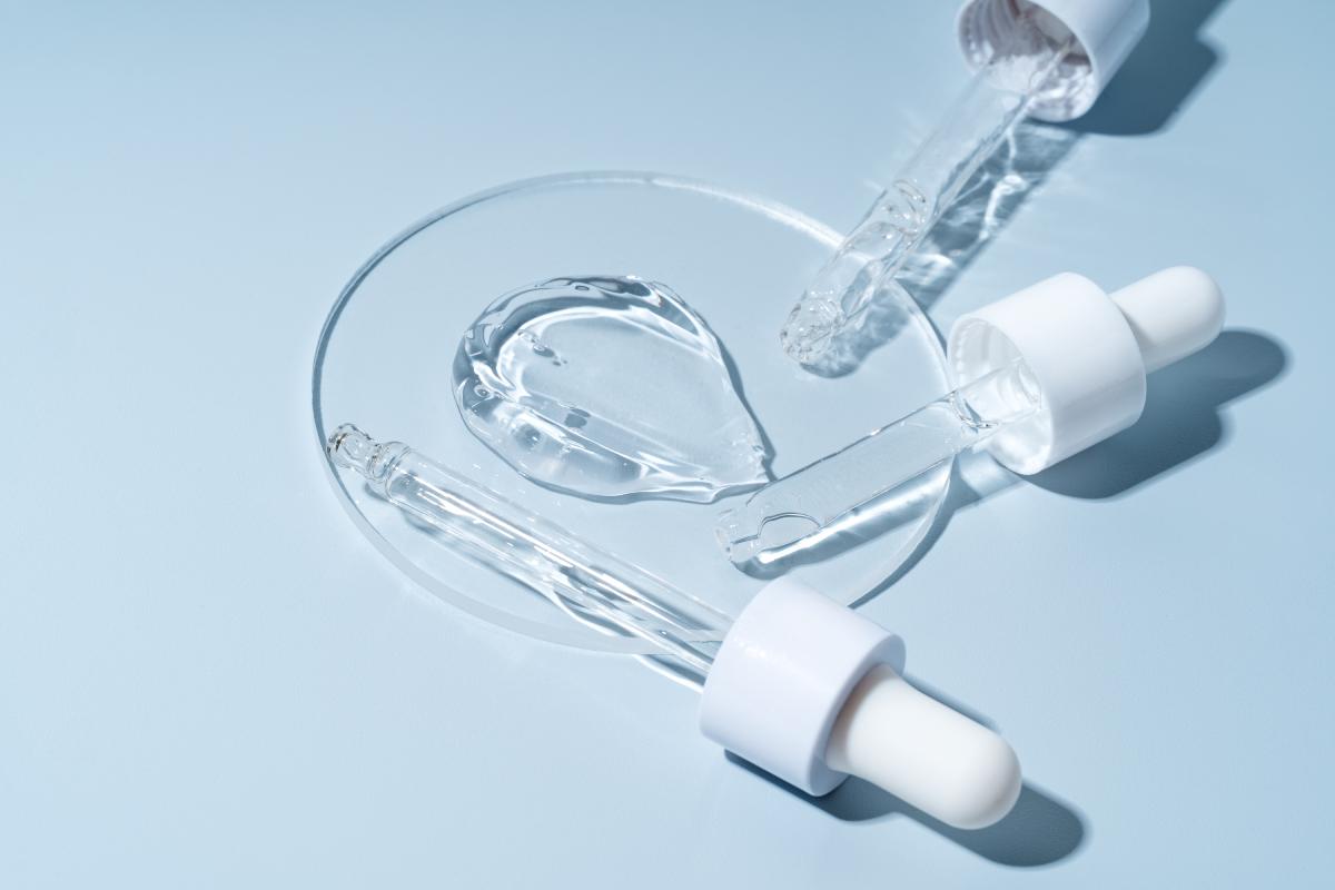 Trois pipettes acide hyaluronique sur un verre circulaire de laboratoire sur fond bleu