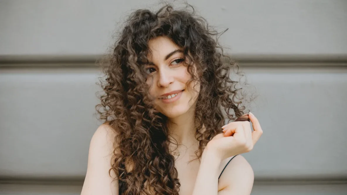 Femme aux cheveux bouclés, souriante, montrant ses magnifiques boucles naturelles