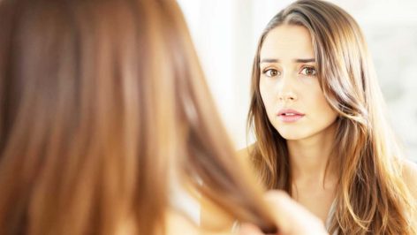 Femme inquiète devant le miroir, examinant ses cheveux