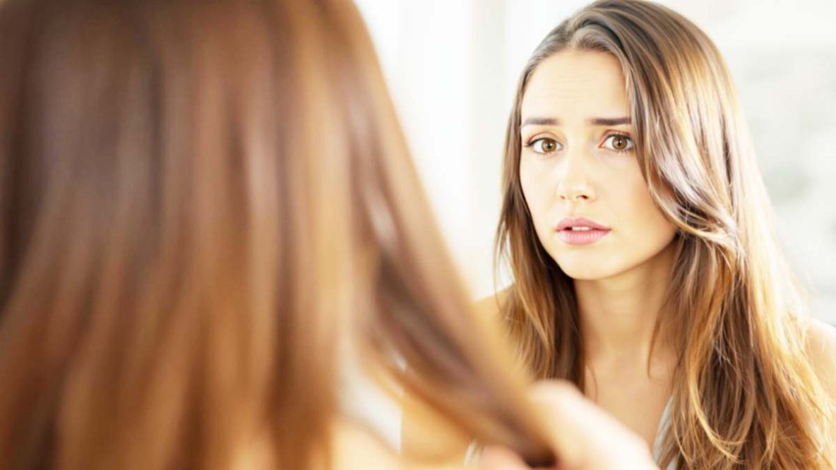 Femme inquiète devant le miroir, examinant ses cheveux