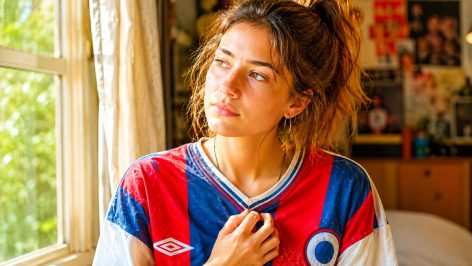 Jeune femme touchant le tissu de son maillot de football vintage, regard nostalgique en gros plan
