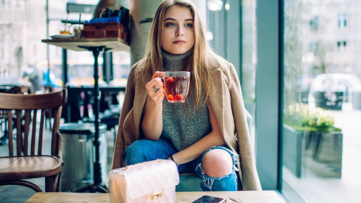 Femme assise confortablement avec une tasse de thé, des livres et des suppléments de vitamines, illustrant le bien-être mental