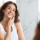 Superbe jeune femme touchant le visage soignant la peau du visage debout près d'un miroir dans une salle de bain moderne à la maison
