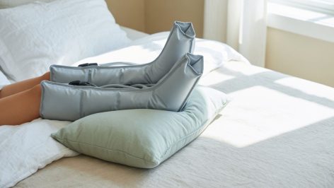 Jambes surélevées équipées de bottes de pressothérapie gonflables sur un lit clair, ambiance bien-etre