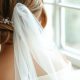 Chignon de mariée vu de dos avec un voile en tulle posé sur du marbre blanc