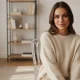 Jeune femme souriante assise sur une chaise Napoléon transparente dans un salon moderne avec lumière naturelle, décoration minimaliste et ambiance chaleureuse. AddictBeaute.com le mag pour les femmes