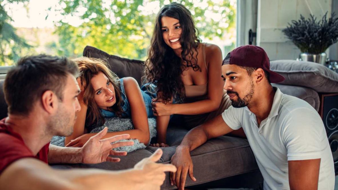 Groupe d’amis souriants posés dans un salon, échangeant des questions coquines dans une ambiance détendue et complice