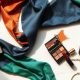 Accorder son maquillage à la couleur de sa tenue : la règle des 3 couleurs Trois tissus colorés et des produits de maquillage assortis posés sur du marbre blanc