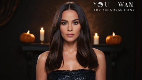 Une promotion beauté à thème Halloween mystérieuse avec un lisseur GHD emballé dans un ruban, accompagné d'une boîte cadeau lumineuse et de décorations d'Halloween comme des citrouilles et des toiles d'araignée.