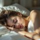 Femme allongée dans des draps blancs, apaisée, illustrant la sérénité et les bienfaits du sommeil nu.