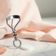 Recourbe-cils en métal et coussinet en silicone posés sur un marbre blanc, pour illustrer le bon geste et l'entretien de l'outil