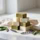 Cubes de savon de Marseille vert olive et crème sur un marbre blanc, linge et feuilles d'olivier, lumière naturelle.