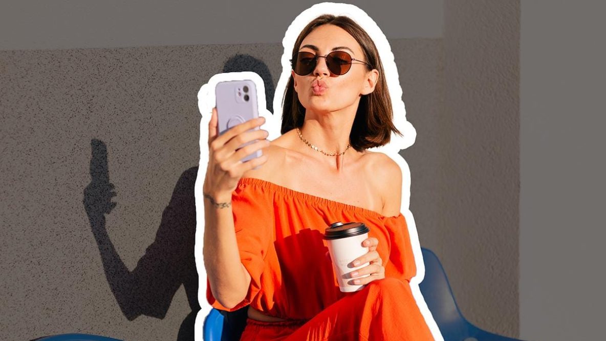 Femme confiante à la coupe courte prenant un selfie, portant une robe orange vif et des lunettes de soleil, tenant un café - parfaite illustration d'une transition capillaire réussie pour la rentrée